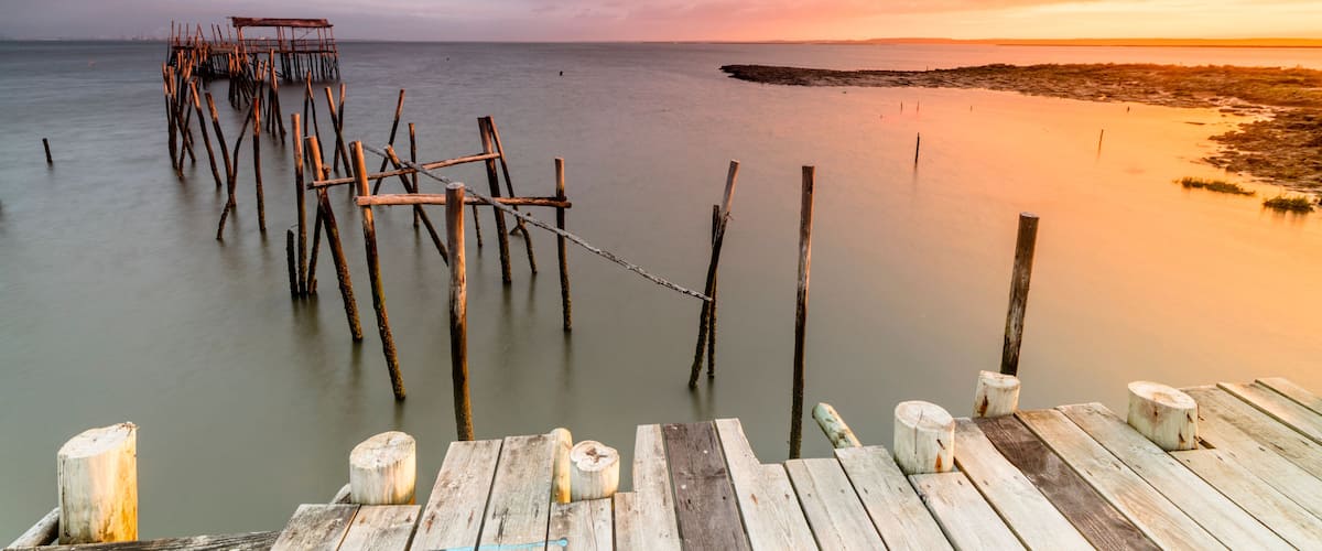 A wooden pier extending into calm waters at sunset.
