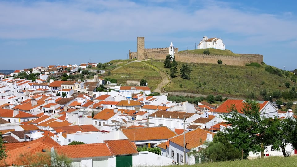 A town with white buildings and red roofs, a hill with a castle, and a church.