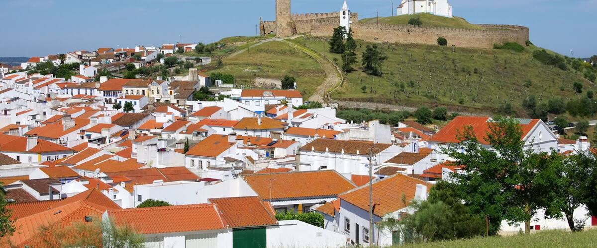 A town with white buildings and red roofs, a hill with a castle, and a church.