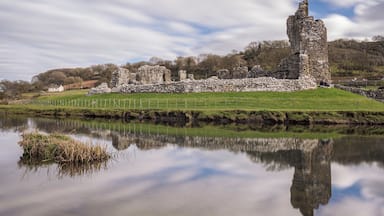 Les ruines d’un château de pierre chargé d’histoire, situé au bord d’un lac paisible dont les eaux reflètent parfaitement le paysage.