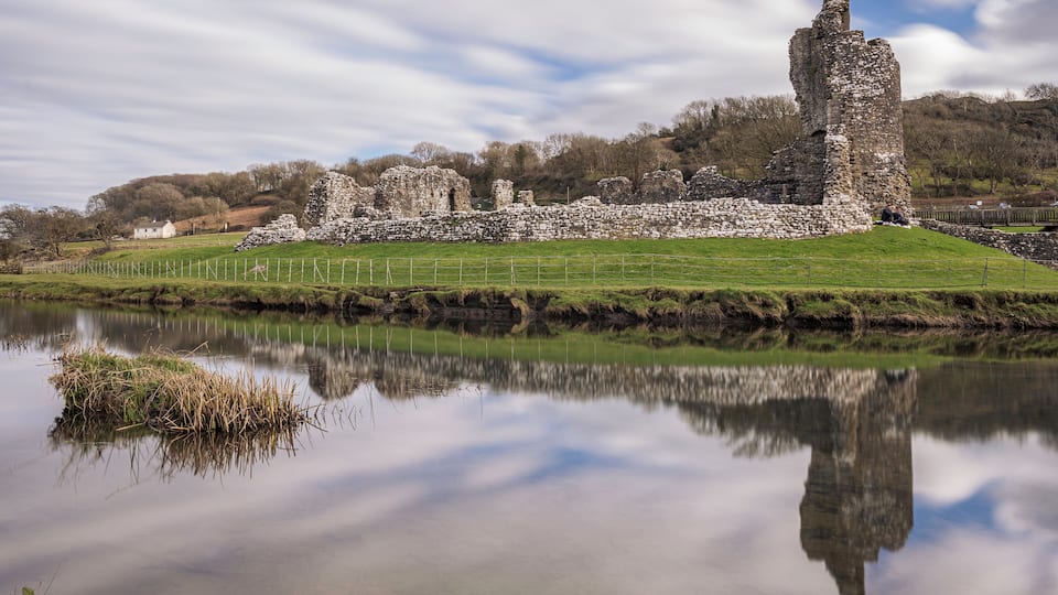 A historic stone castle ruins by a calm lake with a clear reflection.