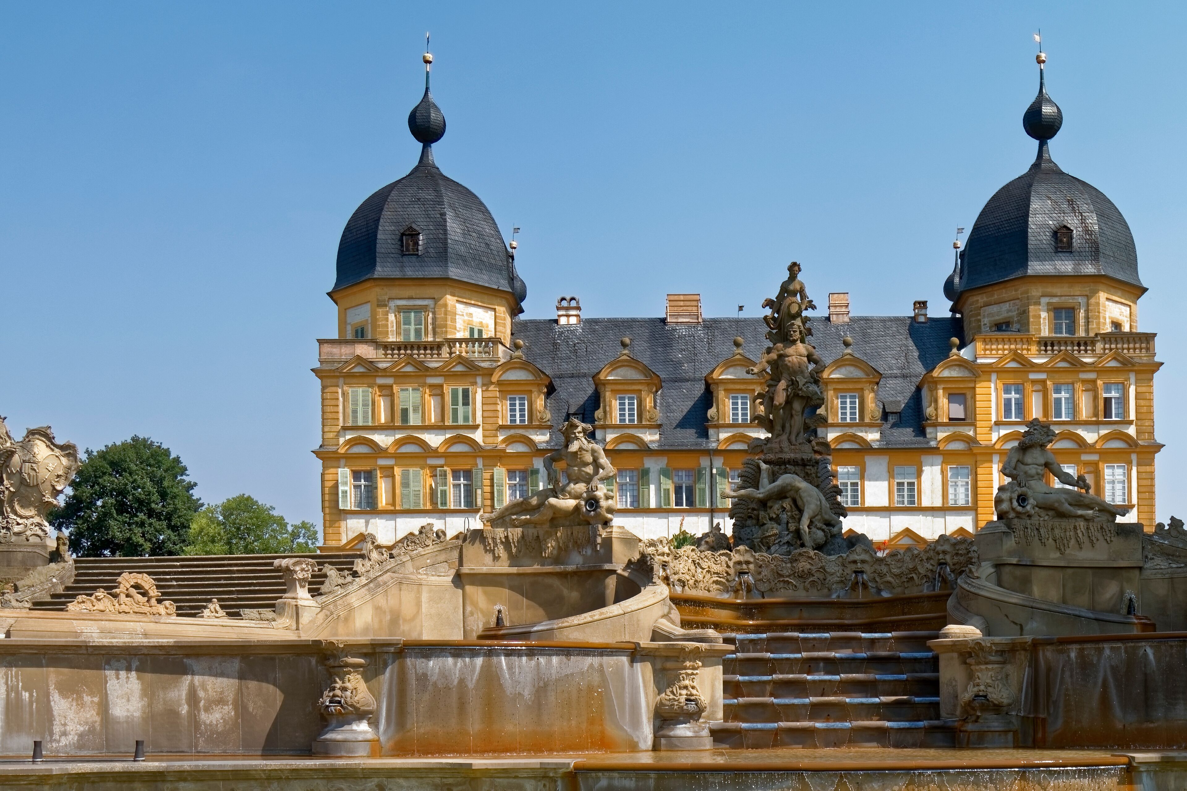 A grand building with two domed towers and a detailed fountain in the foreground.