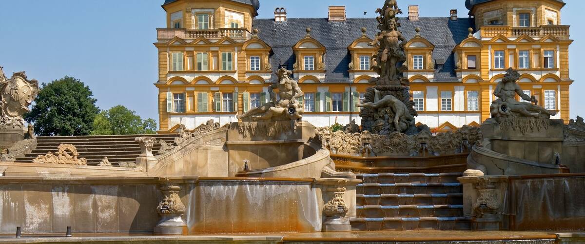 A grand building with two domed towers and a detailed fountain in the foreground.