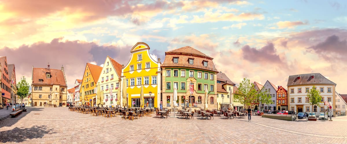 A cobblestone square with colorful buildings, outdoor seating, and a clear sky.