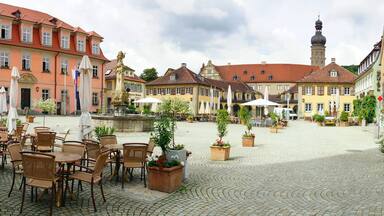 Ein Kopfsteinpflasterplatz mit Außenbestuhlung, historischen Gebäuden und einem Brunnen.