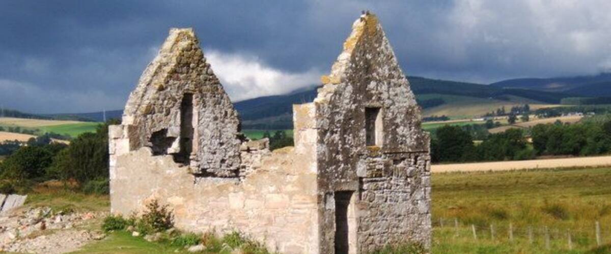 A stone ruin with two triangular roofs in a grassy field.