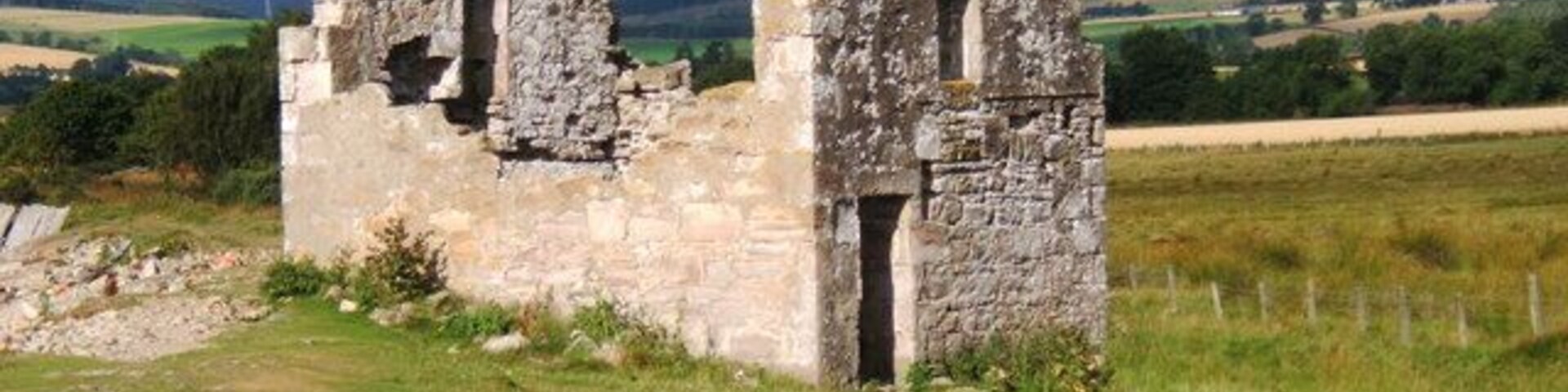 A stone ruin with two triangular roofs in a grassy field.