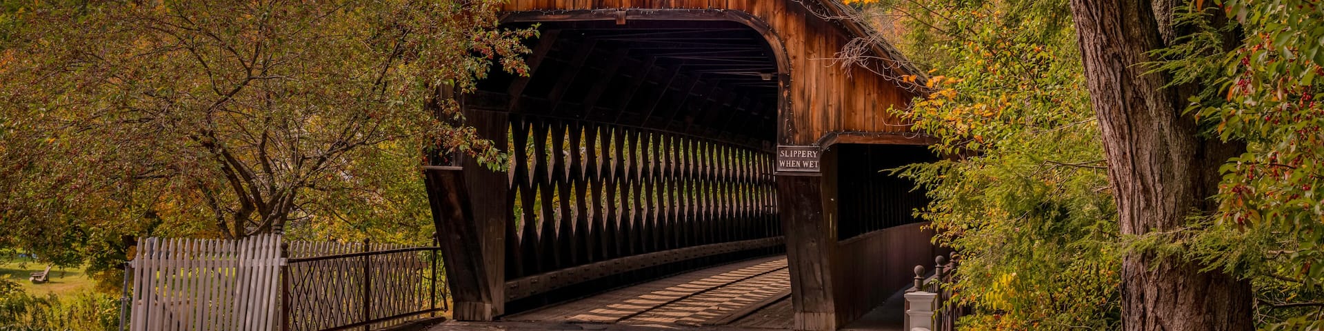A wooden covered bridge with a sign reading 'Slippery When Wet' and a sign above the entrance that says 'Michael's Bridge.'
