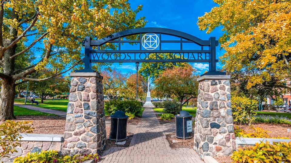 A stone archway with 'WOODSTOCK SQUARE' inscribed above, leading to a pathway flanked by trees and stone pillars.