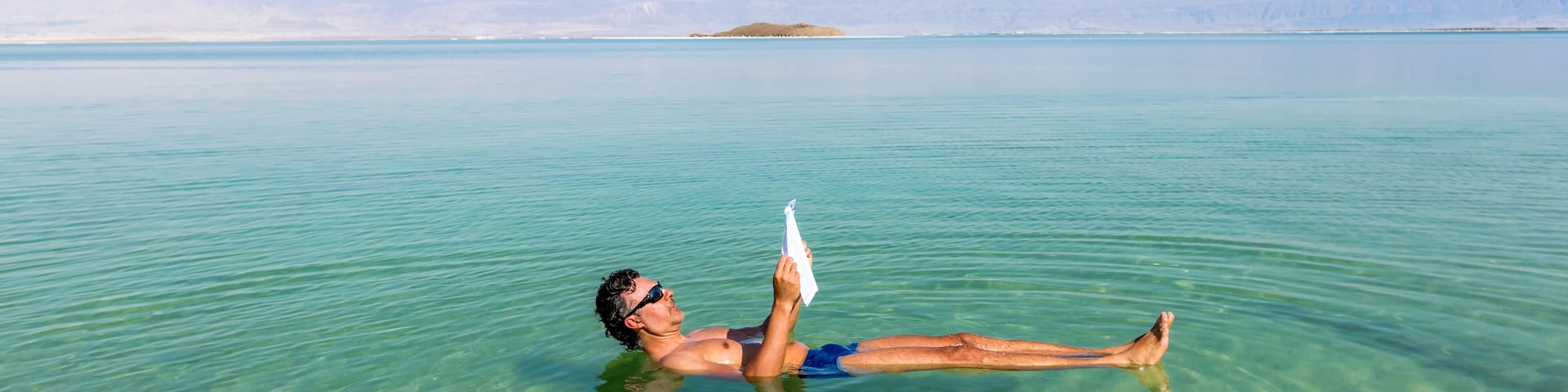 Man relaxing in nature.. View of Dead Sea coastline. Salt crystals at sunset. Texture of Dead sea. Salty sea shore. Web banner in panoramic view.