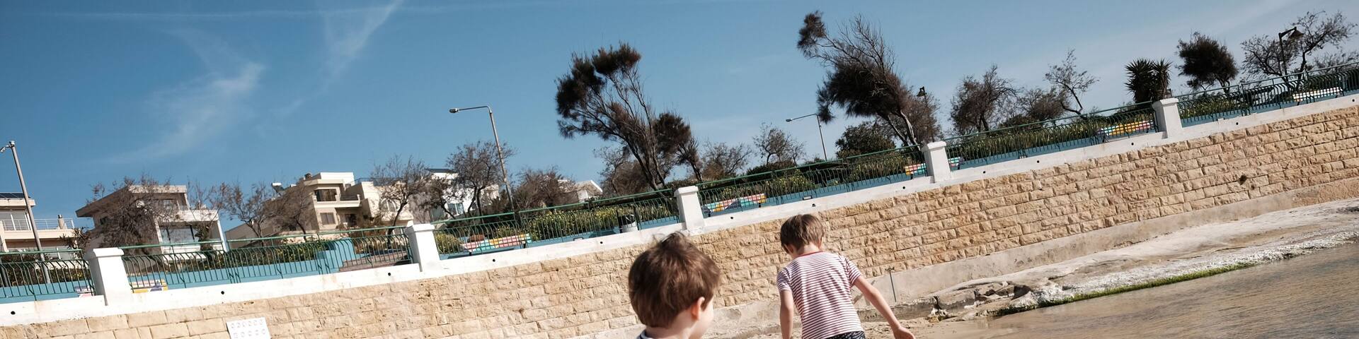 Two children playing on a sandy beach with a stone wall and a fence in the background.