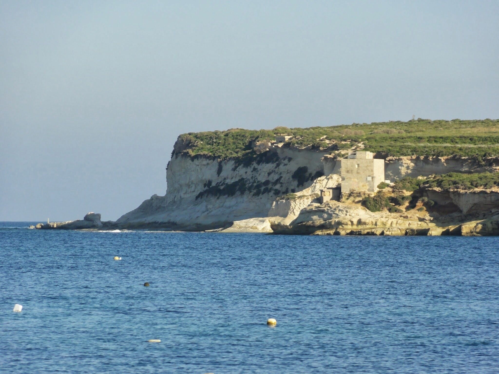 A coastal cliff with a fortified structure and a lighthouse.