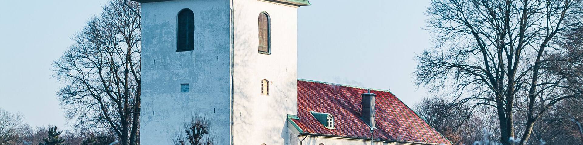 A church with a green roof and a bell tower, surrounded by snow-covered trees.