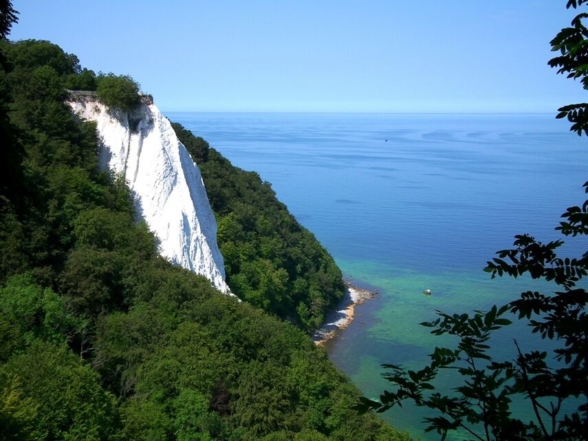 A coastal cliff with a narrow beach and clear blue waters.