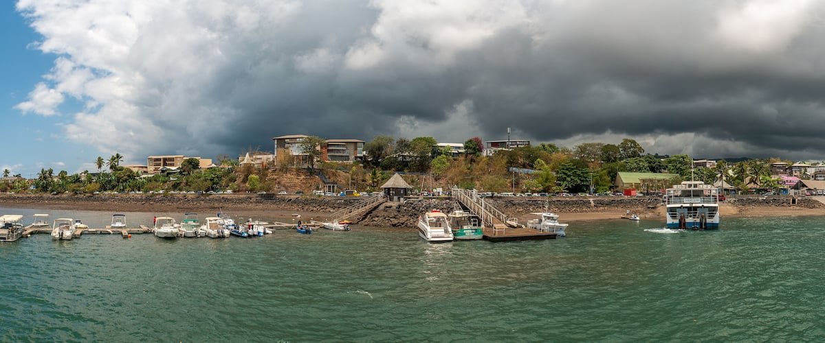 A coastal town with boats docked along the shore, a beach, and a large building in the background.