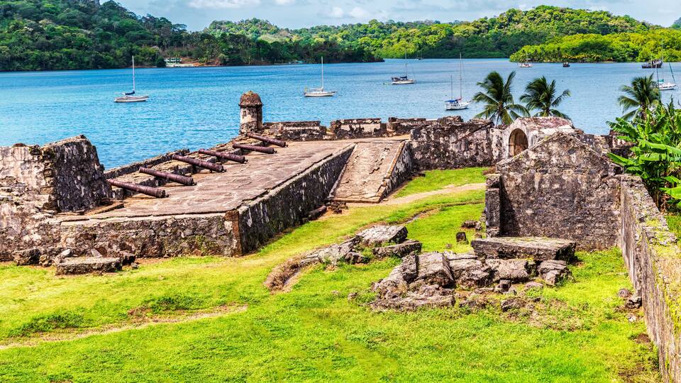 A coastal archaeological site with ruins and a clear view of the ocean with boats.