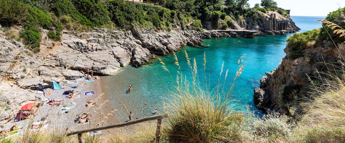 Un paisaje costero con una playa, acantilados rocosos y un edificio en una ladera.
