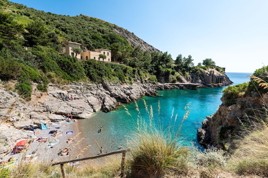 Un paisaje costero con una playa, acantilados rocosos y un edificio en una ladera.