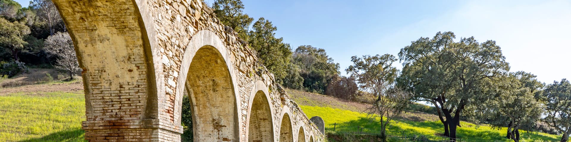 A series of stone arches in a grassy field with a clear sky.