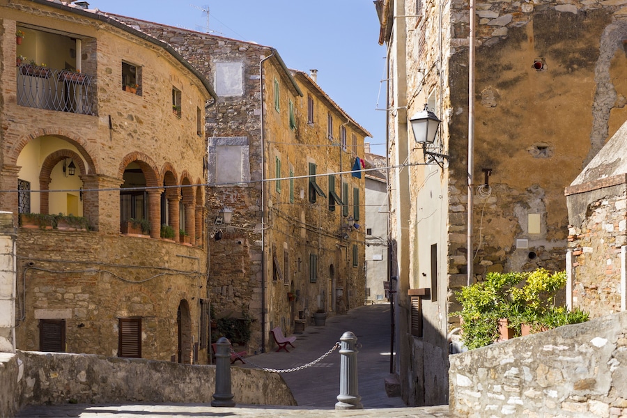 Una stretta via con edifici in pietra, portali ad arco e una recinzione in rete metallica.