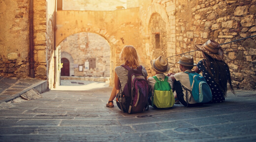 Mother and kids tourists sightseeing beautiful Italian town of Campiglia Marittima. Sunny summer day. Italy, Tuscany.