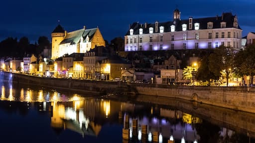 A nighttime river scene with a stone bridge, illuminated buildings, and a castle-like structure.