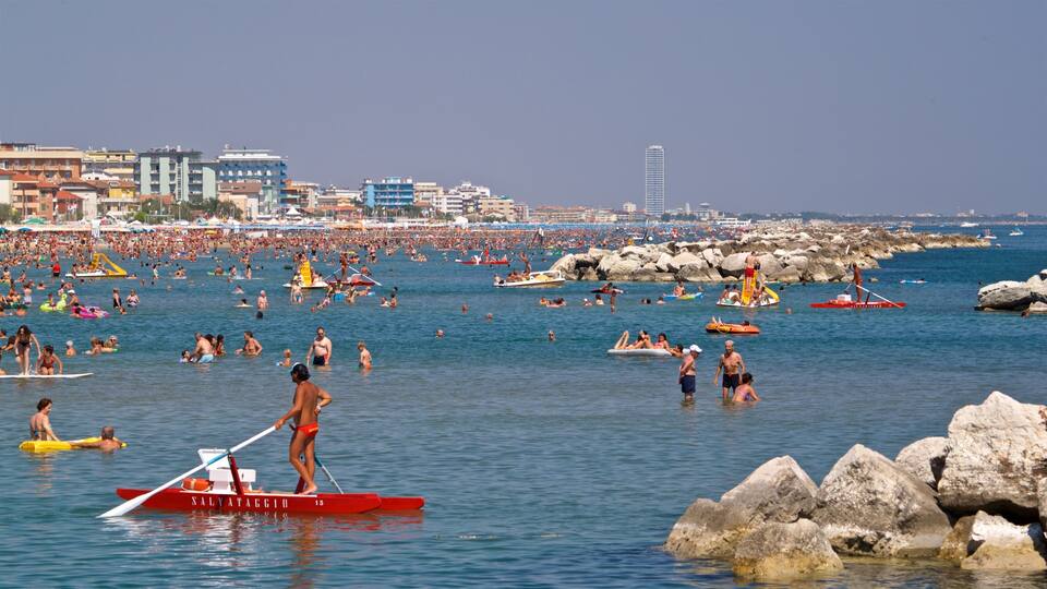 A crowded beach with people swimming and using various watercraft.