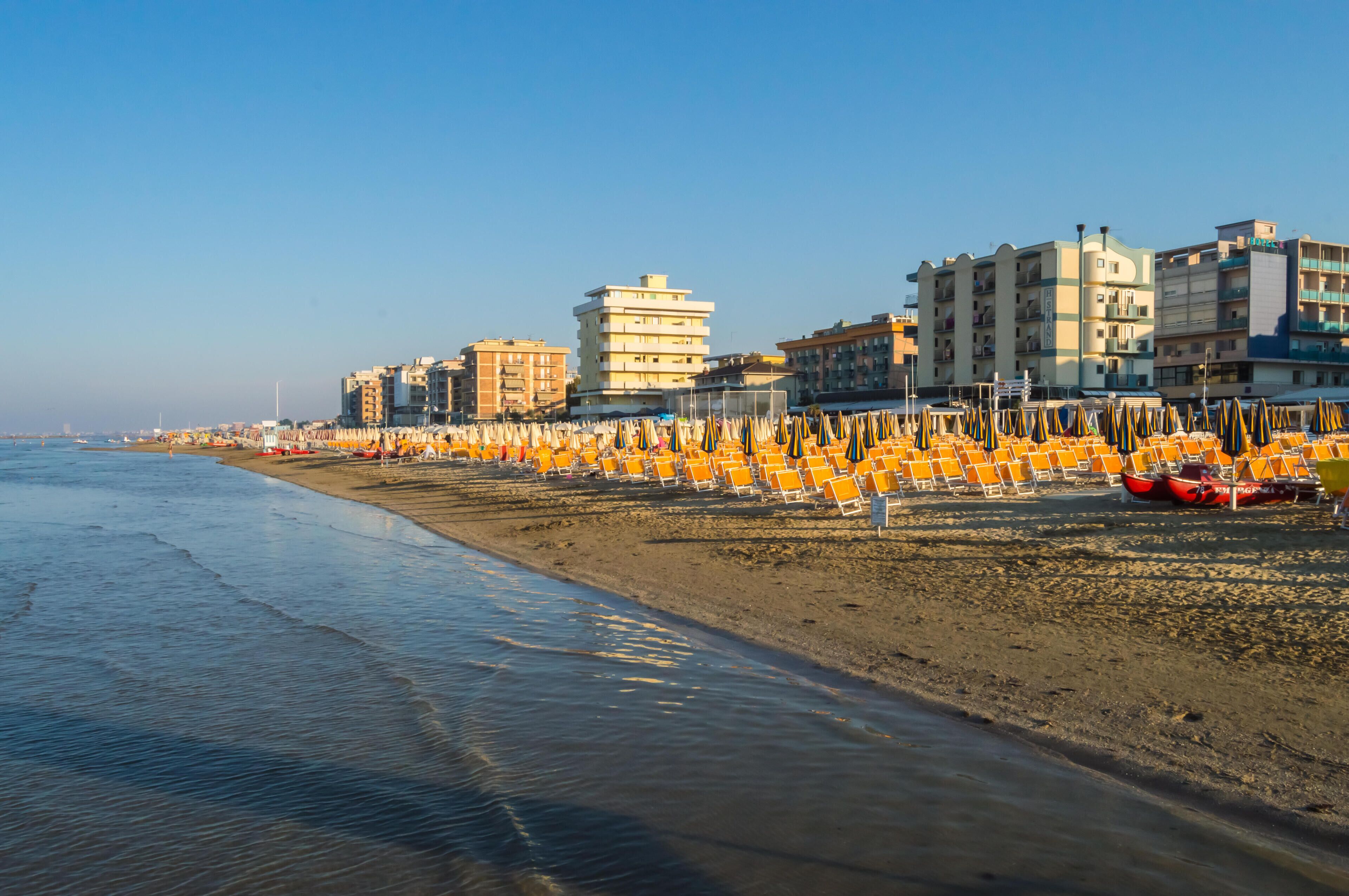 A beach with rows of orange chairs and a row of buildings along the shoreline.