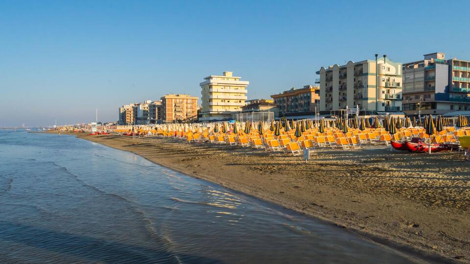 A beach with rows of orange chairs and a row of buildings along the shoreline.