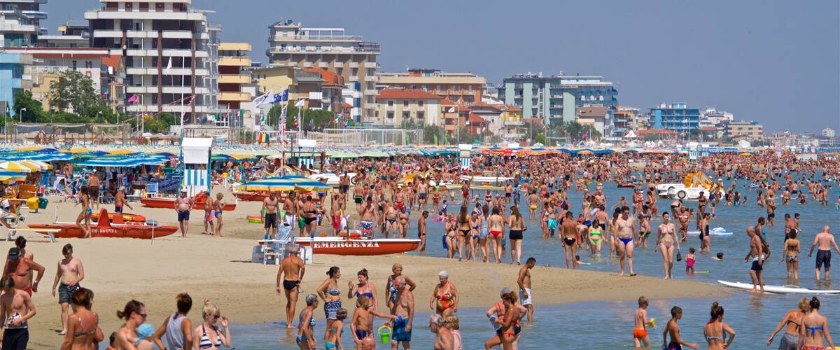 A crowded beach with people in swimsuits, umbrellas, and boats.