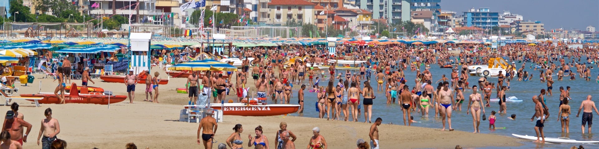 A crowded beach with people in swimsuits, umbrellas, and boats.