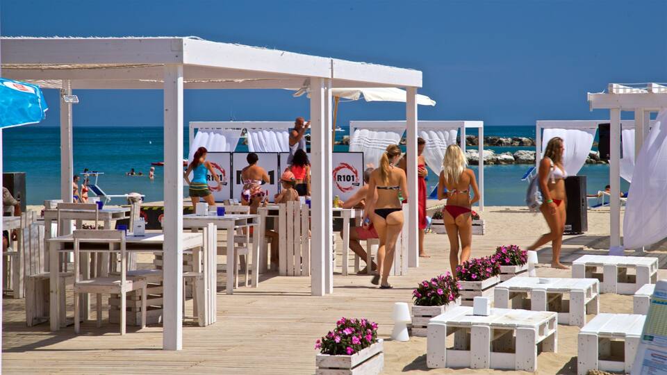 A beachside event with wooden tables and white tents, people in swimwear, and a clear blue sky.