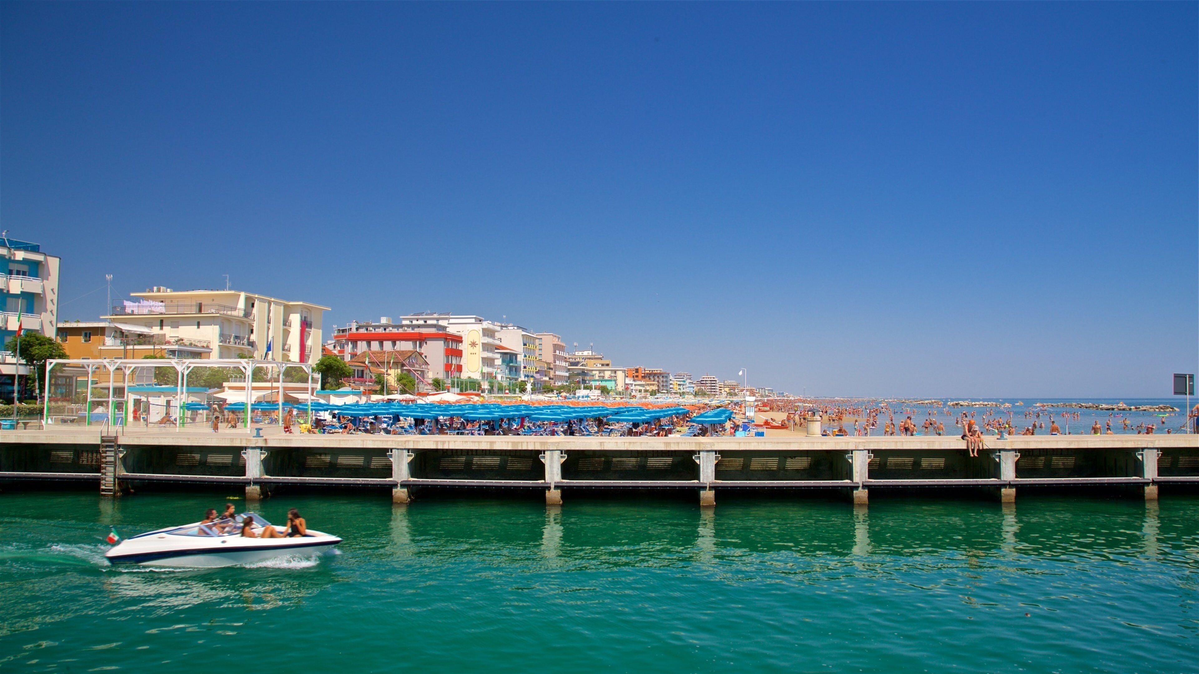 Uma cidade costeira com um cais, um barco e uma praia com guarda-sóis.