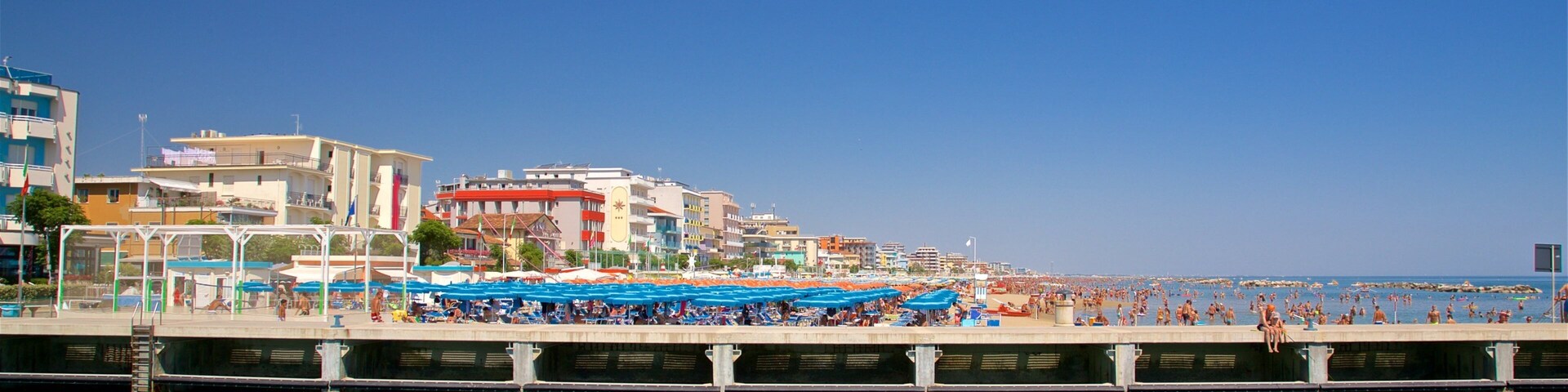 Uma cidade costeira com um cais, um barco e uma praia com guarda-sóis.