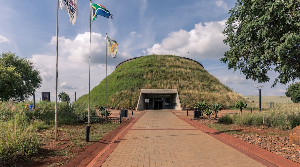 A pathway leading to a hilltop structure with flags, surrounded by greenery and trees.