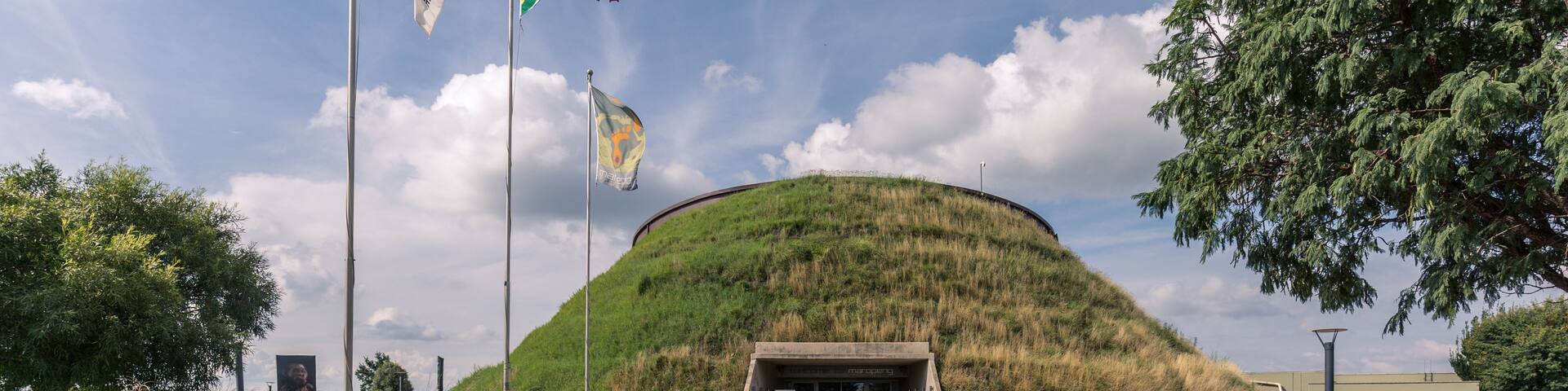 A pathway leading to a hilltop structure with flags, surrounded by greenery and trees.