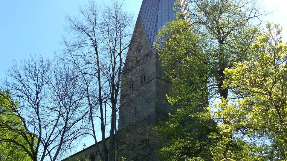 A tall, pointed tower with a spire, surrounded by trees and a stone wall.