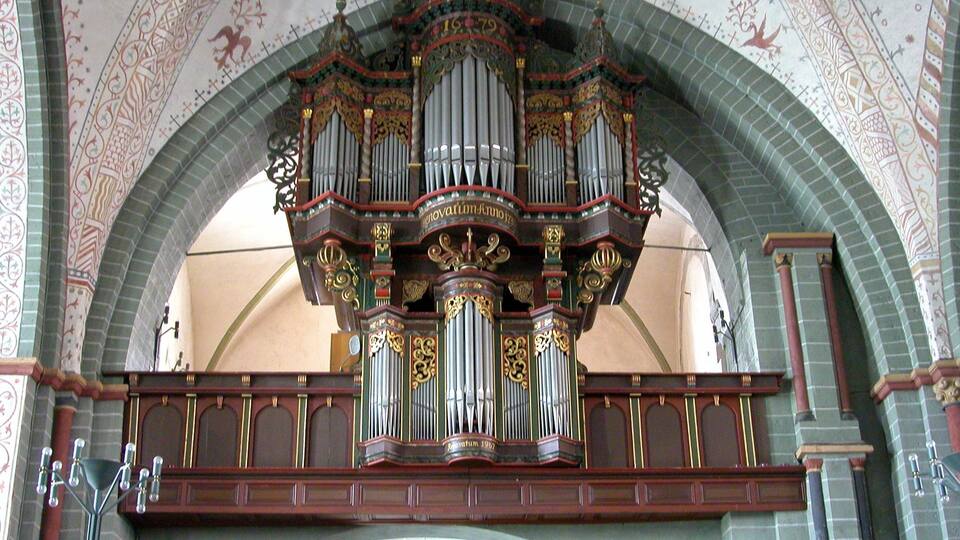 An ornate pipe organ with intricate designs and a large arched ceiling with decorative patterns.