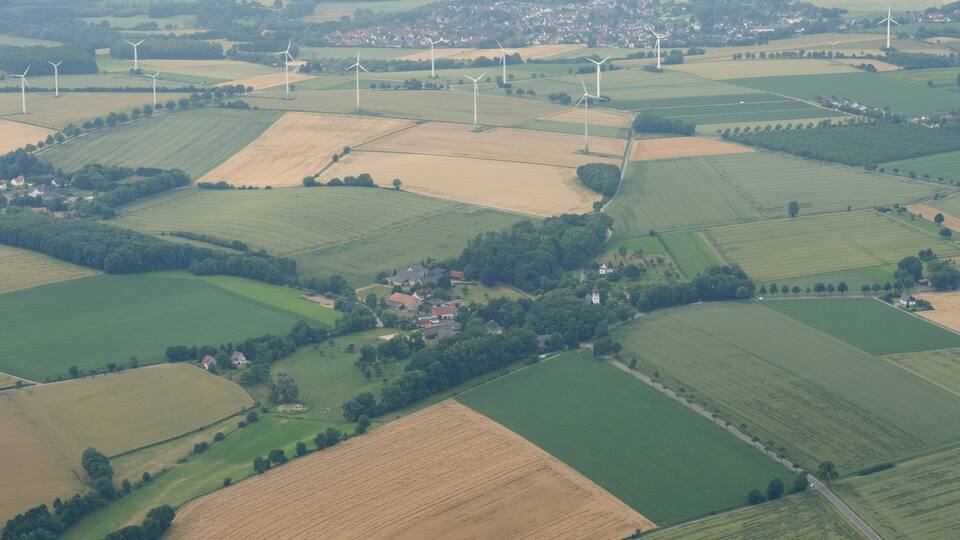 An aerial view of a rural landscape with wind turbines, fields, and a small village.