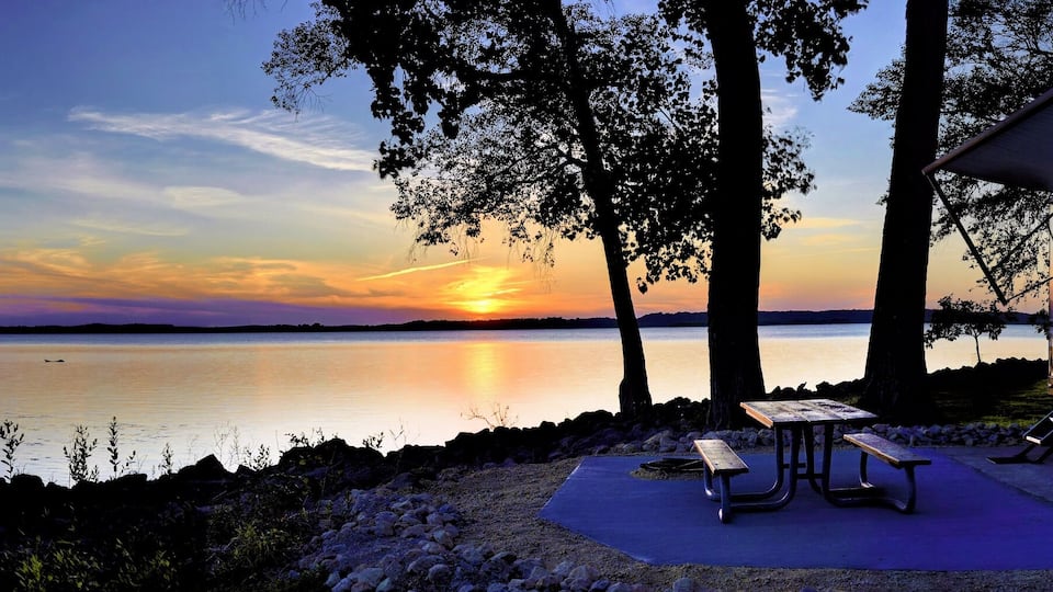 A lakeside campsite with a tent and picnic table at sunset.