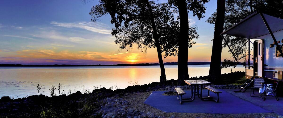 A lakeside campsite with a tent and picnic table at sunset.