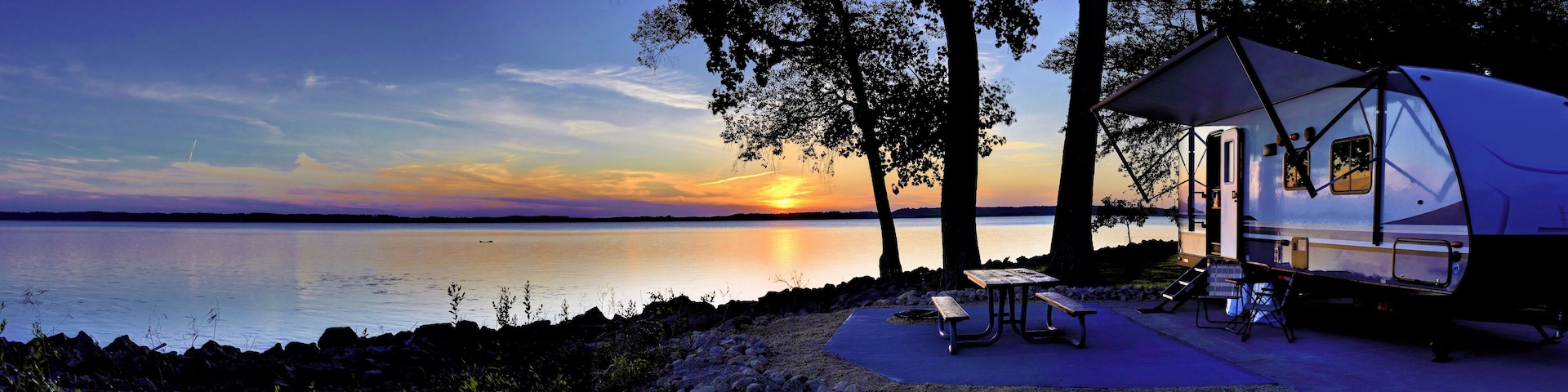 A lakeside campsite with a tent and picnic table at sunset.