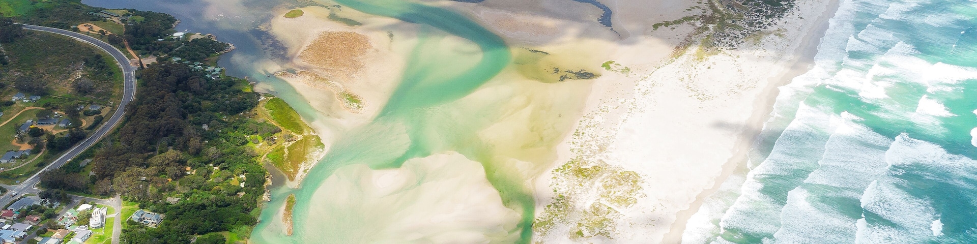 Vista aérea de una zona costera con playa, aguas azules cristalinas y una combinación de vegetación verde y urbanización.
