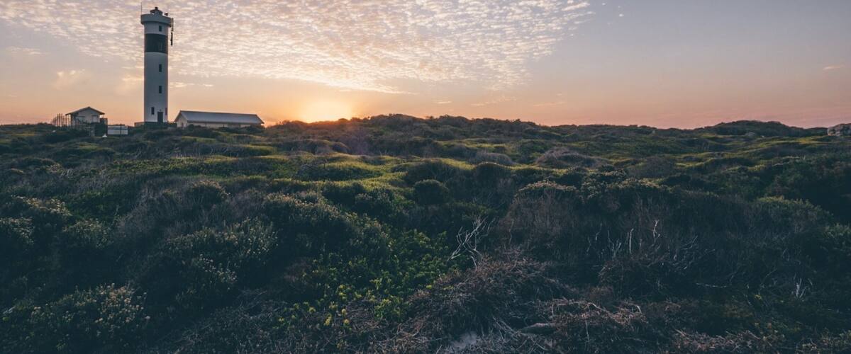 A lighthouse on a hill with a sunset and scattered clouds.