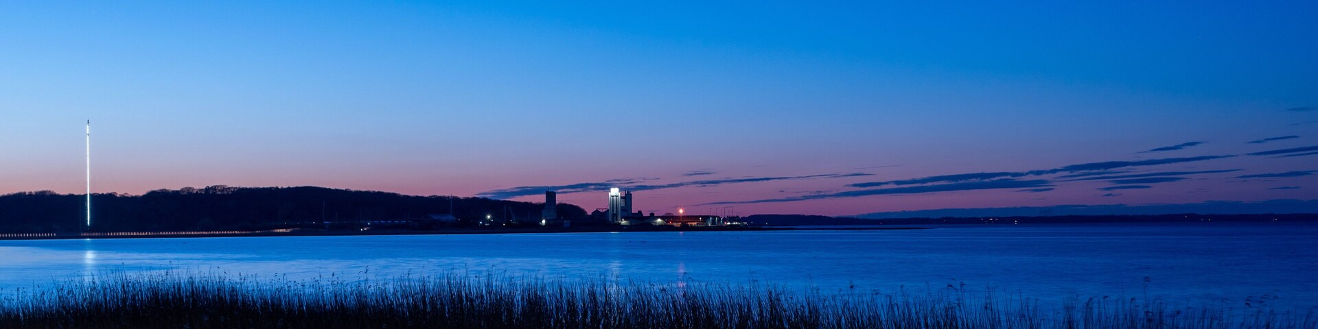 A calm body of water with a city skyline in the distance, featuring a prominent tower and several buildings.