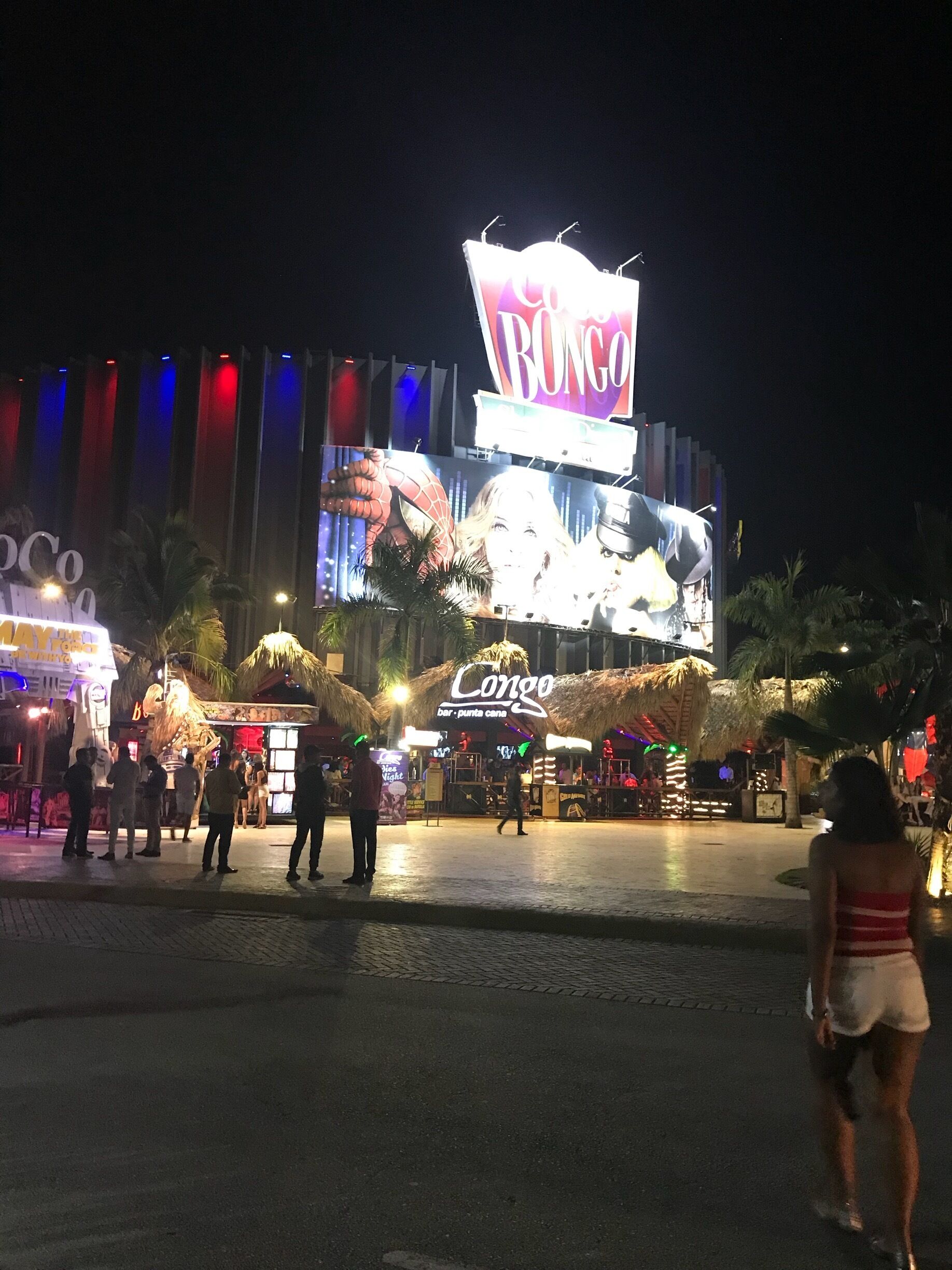 Cena noturna em um cassino com letreiros iluminados e palmeiras.