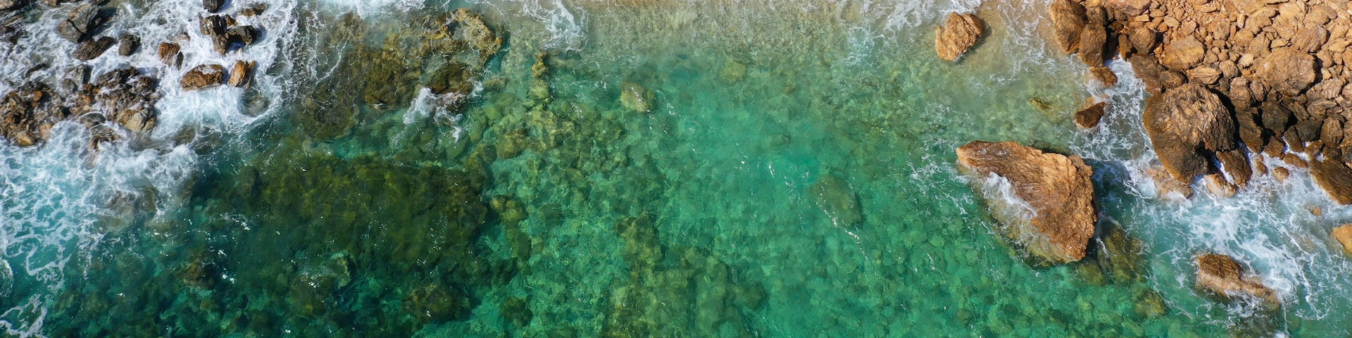 A rocky coastline with clear turquoise waters and a sandy beach.
