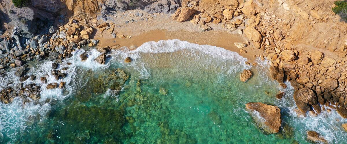A rocky coastline with clear turquoise waters and a sandy beach.