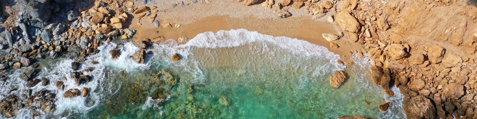 A rocky coastline with clear turquoise waters and a sandy beach.