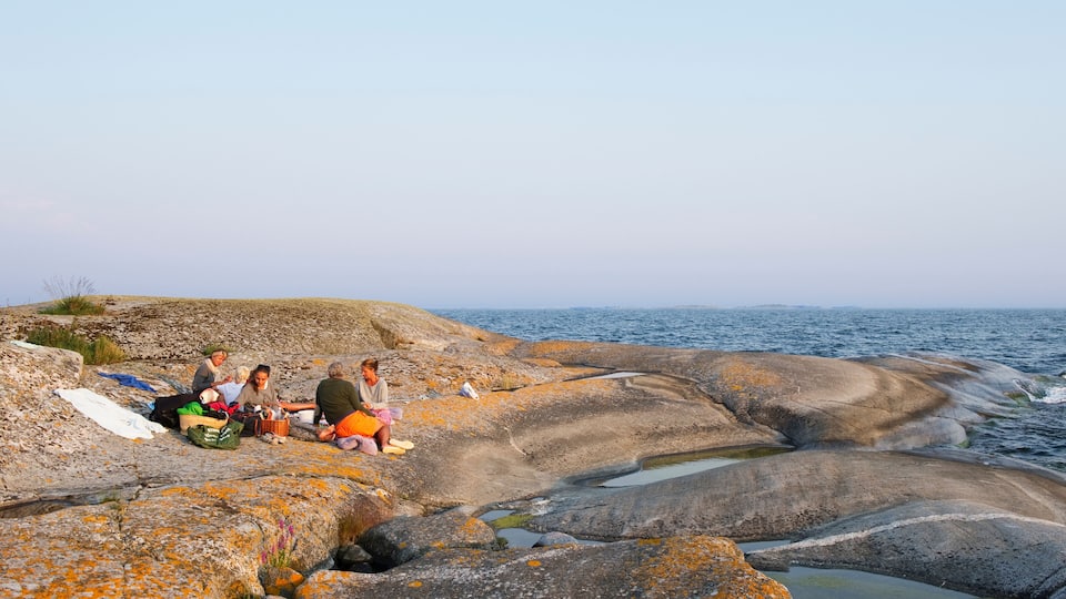 A group of people sitting on rocky terrain near a body of water.